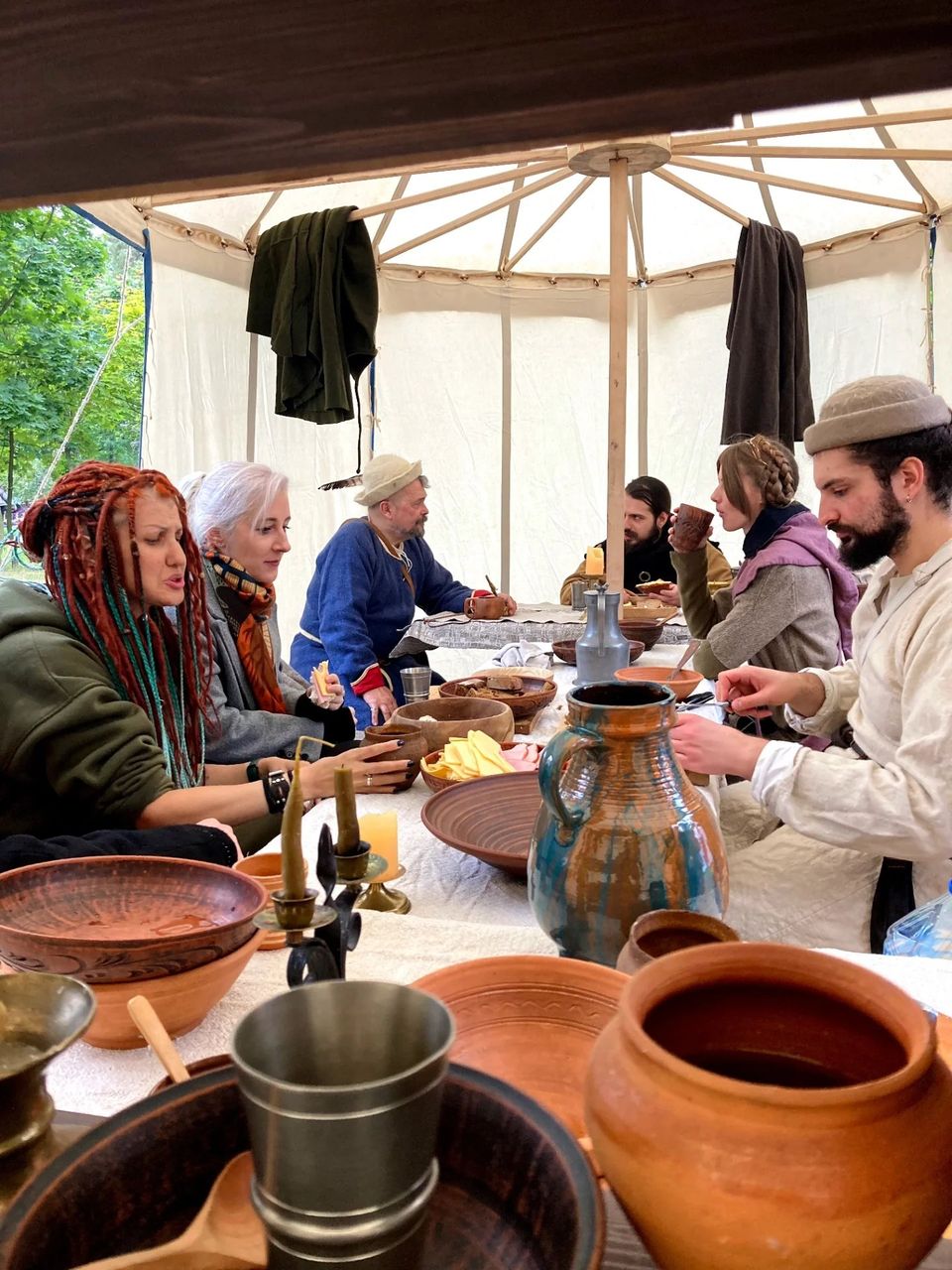 Reenactors in medieval clothing at a camp table with ceramics, jugs and food inside a tent at the Museum of Kyiv History food festival, 2025