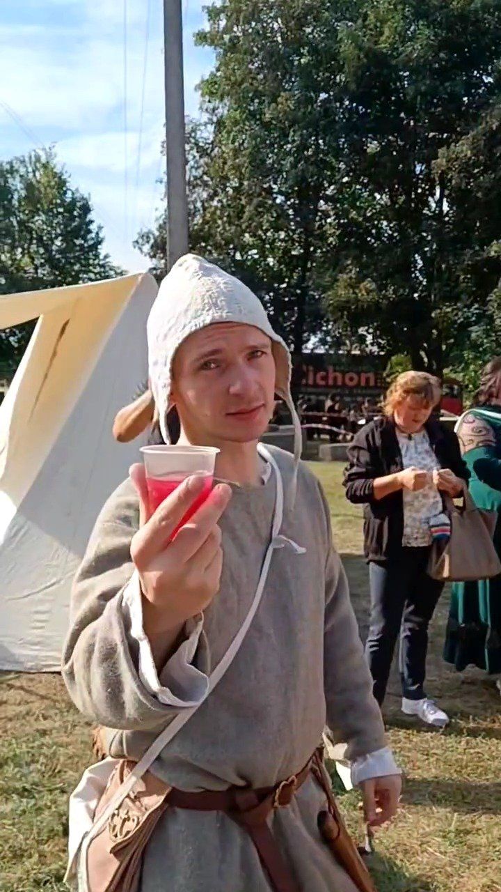 An Atira Ruthenia reenactor in a linen hood and medieval tunic holding a cup of red kysil at the festival